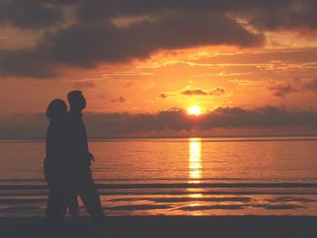 Silhouette people on beach against sky during sunset