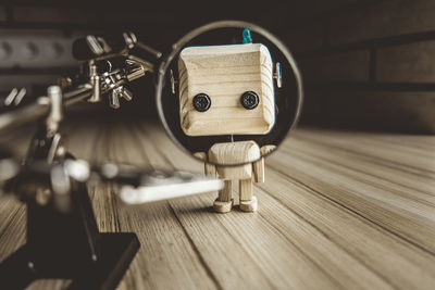 Wooden robot android stands on a table under a magnifying glass. metal clamps with magnifying glass