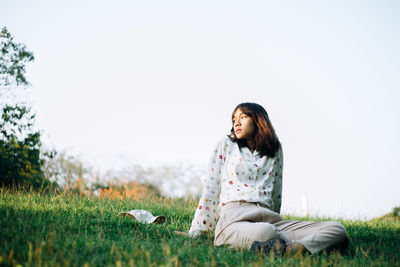 Woman sitting on field against sky