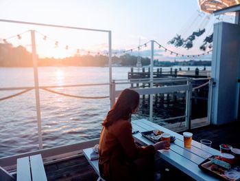 Woman drinking beer while sitting by sea against sky