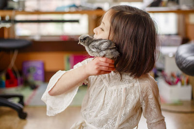 A beautiful little girl in lace dress holds baby chick up to her cheek