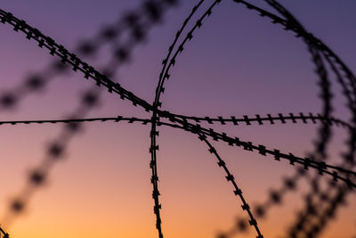 Close-up of barbed wire against sky at sunset