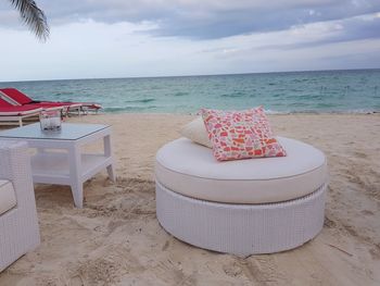 Chairs and table at beach against sky