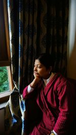 Young woman looking through window at home