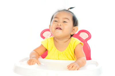 Cute baby girl sitting on high chair against white background