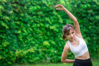 Young woman with arms raised standing against plants