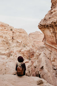 Rear view of young woman with backpack sitting on rock at desert against sky