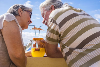 Senior couple drinking cocktail on retaining wall against sky