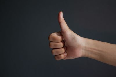 Cropped hand showing thumbs up sign against black background