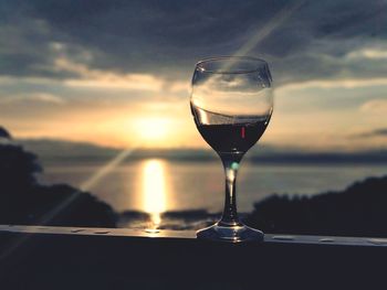 Close-up of wineglass against sky during sunset