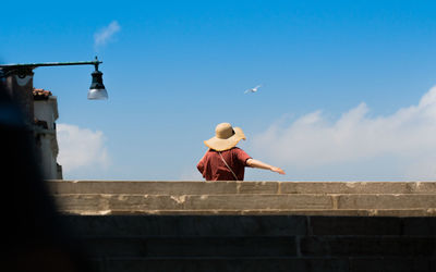 Low angle view of woman wearing hat while standing on rooftop against sky