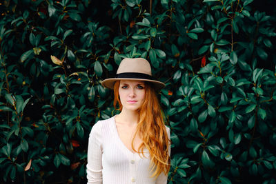 Portrait of beautiful young woman standing against plants