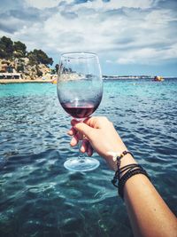 Close-up of woman hand holding drink at sea against sky