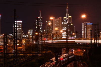 Illuminated railroad tracks in city against sky at night