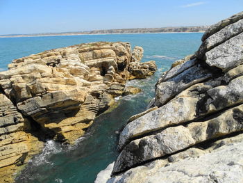 Rock formation by sea against clear sky