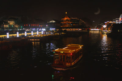 Illuminated buildings by river against sky in city at night