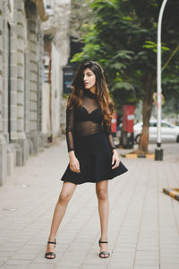 Full length portrait of young woman wearing black dress in city