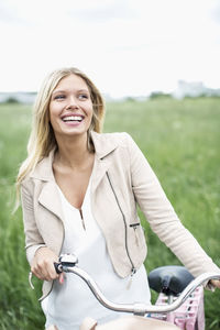 Happy young woman with bicycle looking away while standing at field