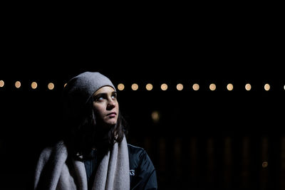 Young woman looking up while standing outdoors at night