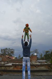 Teenage boy catching younger brother while standing against sky