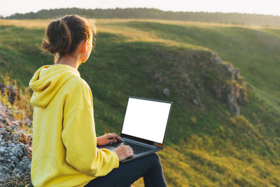 Crop photo of young woman traveler freelancer in yellow hoodie with white screen opened laptop 