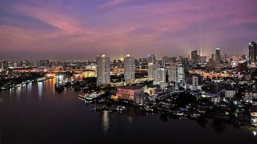 Illuminated cityscape by river against sky at night