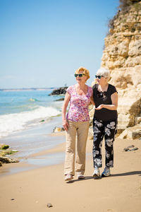 Two elderly women are walking along the rocky shore