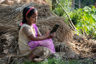 A rustic teenage girl is sitting alone in a rural environment with an android phone