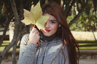 Close-up portrait of smiling young woman holding leaf