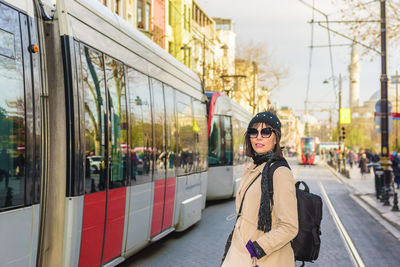 Portrait of woman standing by cable car on road in city