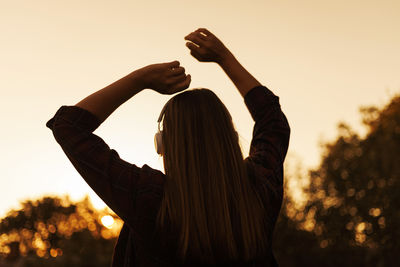 Low angle view of woman gesturing against sky during sunset