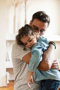 Father embracing sad daughter while standing at home