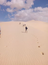 People moving up on sand dune in desert against sky