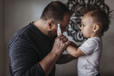 One year old boy taking father’s temperature at home during isolation
