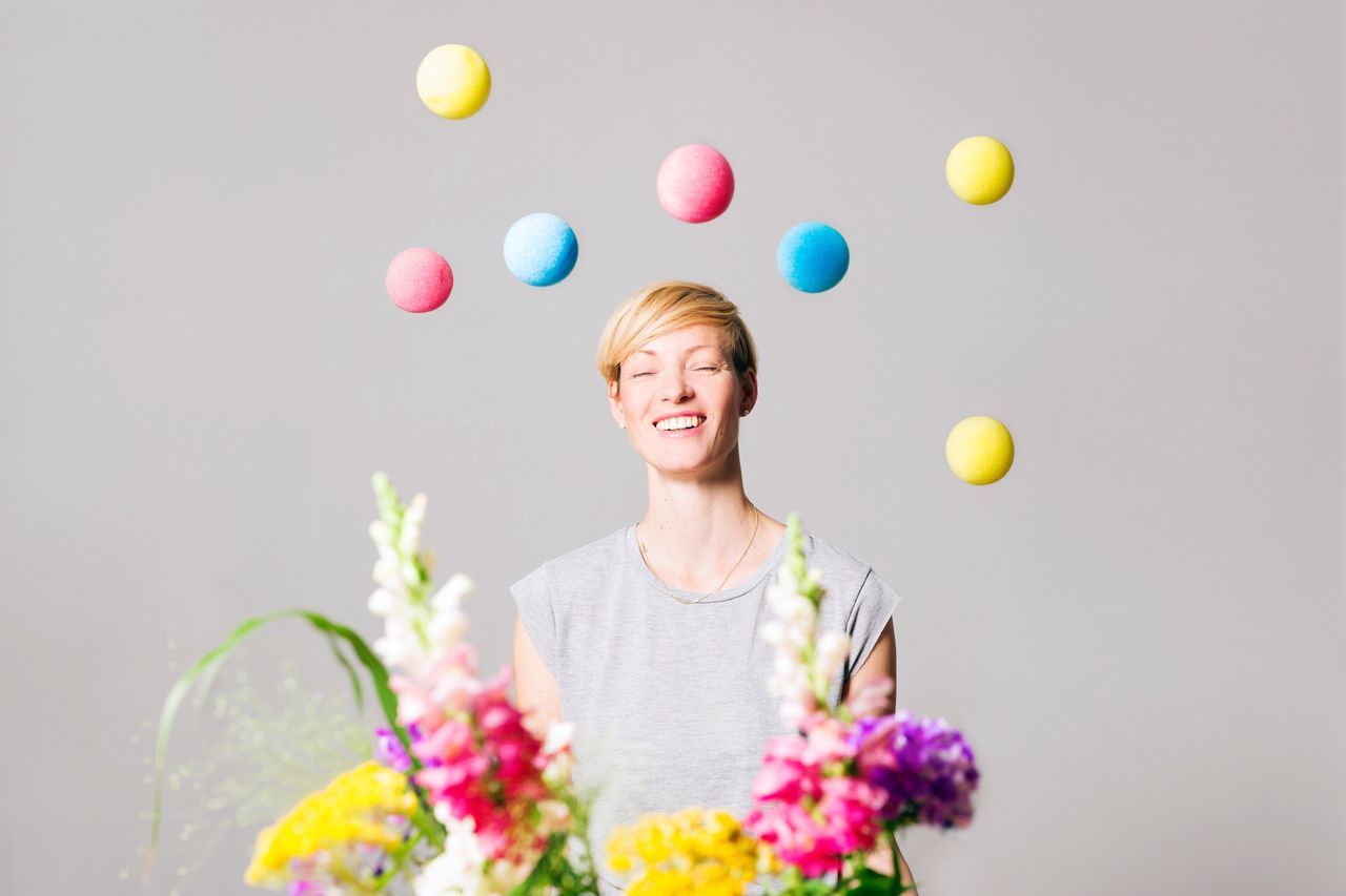 flower, front view, one person, real people, smiling, young adult, balloon, looking at camera, young women, casual clothing, happiness, portrait, holding, fragility, standing, multi colored, studio shot, one young woman only, gray background, blond hair, lifestyles, beautiful woman, freshness, day, one woman only, indoors, florist, adult, adults only, people