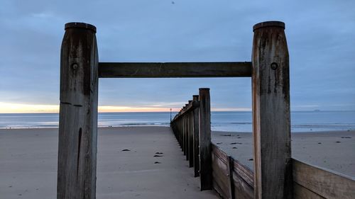 Wooden posts on beach against sky during sunset