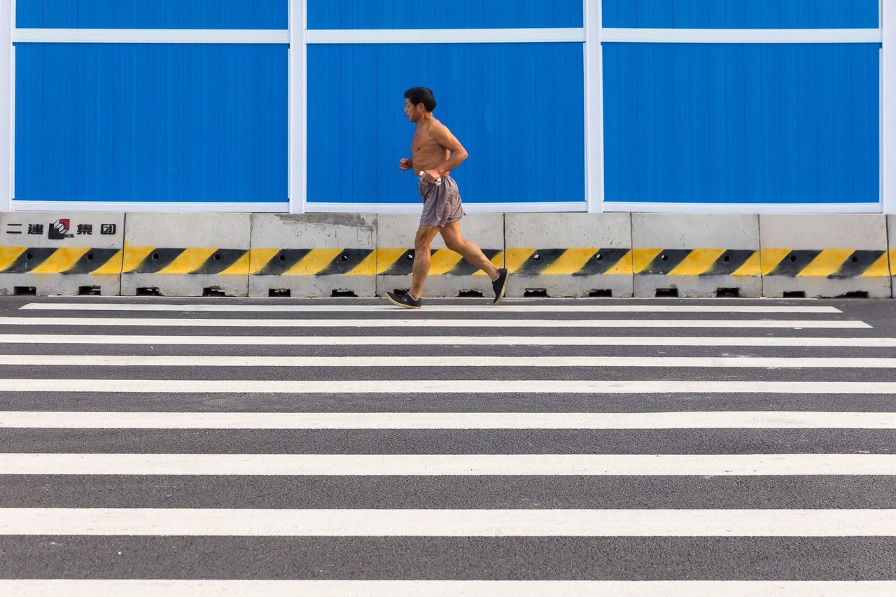 full length, symbol, road marking, one person, crosswalk, crossing, city, road, zebra crossing, marking, real people, sign, walking, transportation, day, architecture, casual clothing, striped, lifestyles, outdoors