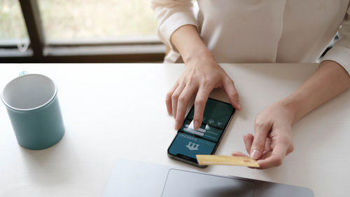 Midsection of woman using mobile phone while sitting on table