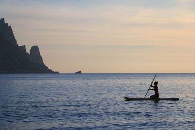 Woman paddleboarding in sea against sky during sunset