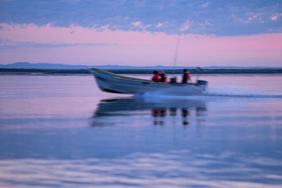 People in sea against sky during sunset