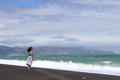 Girl in profile on the beach with waves touching the black sand