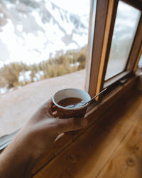 Cropped hand having coffee against window