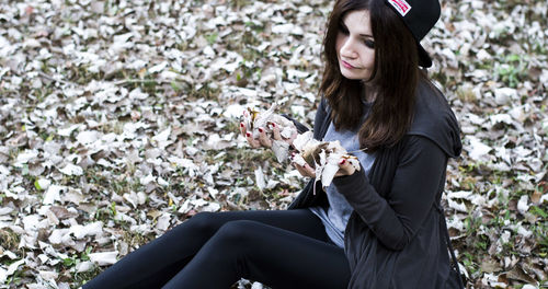 High angle view of woman holding dry leaves while sitting on field during winter