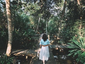 Rear view of woman walking on footbridge in forest