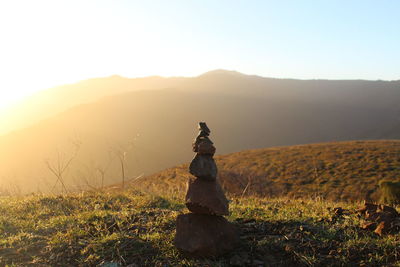 Stack of stones on hill against sky during sunny day