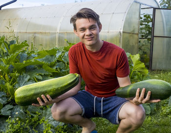 Portrait of young man holding vegetables while crouching in garden