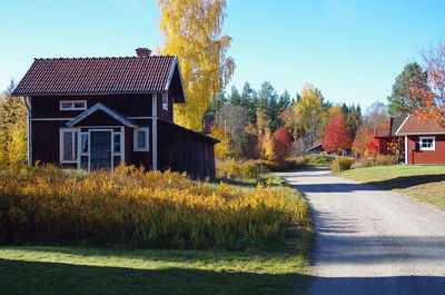 House and trees by road against clear sky