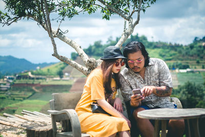 Couple using smart phone while sitting against sky