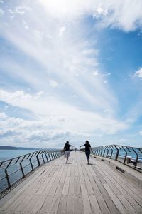 People on pier at sea against sky