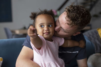 A biracial toddler pointing while her father kisses her cheek